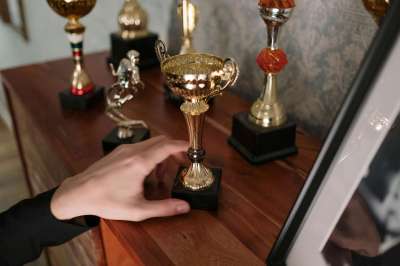 pexels-photo-6565255-6565255 A close-up of a hand reaching for a shiny trophy on a wooden shelf, symbolizing success.